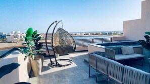 Une terrasse sur le toit avec un fauteuil suspendu, un espace salon et des plantes en pot.