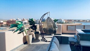 A rooftop terrace with a hanging chair, potted plants, and a view of the beach and buildings. - El-Gouna Gem
 Tranquil 3-bedroom apartment with AC in Red Sea Governorate (Hurghade 2)