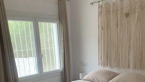 Ein Schlafzimmer mit Bett, Vorhängen, einem Fenster und einem Wandbild.