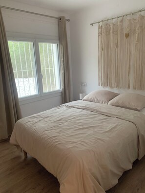 A bedroom with a bed, curtains, a window, and a wall-mounted decorative piece. - Maison à la Mer 8 pers. 60 kms Perpignan (CT)