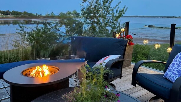 Een terras met buitenmeubilair, een vuurkorf en uitzicht op het water.