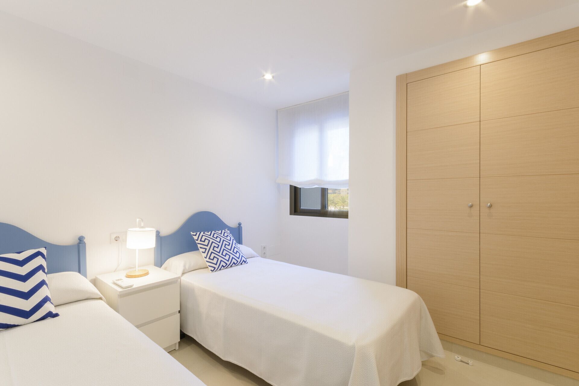 Une chambre avec deux lits, une table de chevet avec une lampe, une fenêtre donnant sur un beau paysage et une grande armoire.