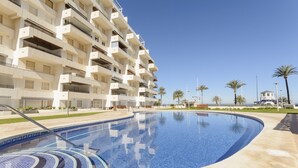 A swimming pool with a tiled edge, surrounded by a building with multiple balconies and a clear sky. - AG DUPLEX 2-3 PREMIUM - only families (Playa de Gandía)
