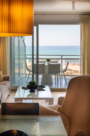 A modern living room with a glass coffee table, a sofa, and a view of the beach through large windows. - FRONTAL AL MEDITERRANEO - only families (Playa de Gandía)