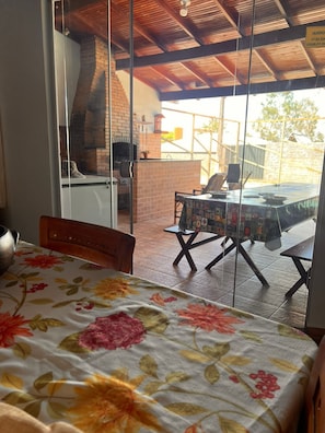 A room with a bed, a table with a floral tablecloth, a brick fireplace, and a view of an outdoor patio area. - Ranch for fishing and relaxing in Carlópolis (Carlópolis)