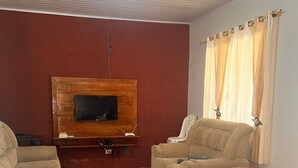 Ein Wohnzimmer mit Fernseher, zwei Sofas, einem Esstisch und Holzboden.