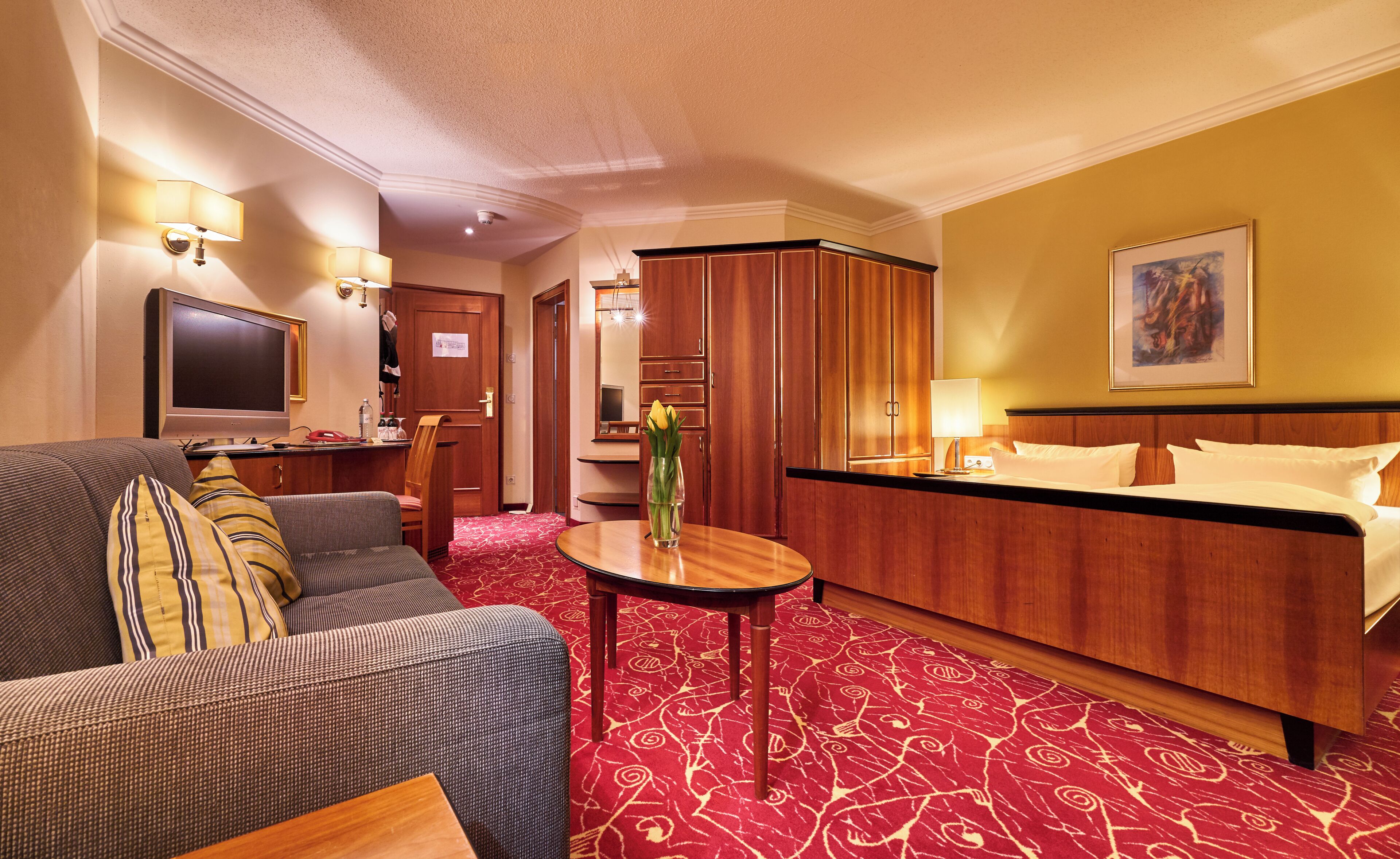 Habitación de hotel con sofá, televisión, escritorio con computadora, cama y armario de madera.