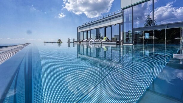 Un edificio moderno con fachada de vidrio, una zona de piscina con sillones de descanso y un cielo despejado.