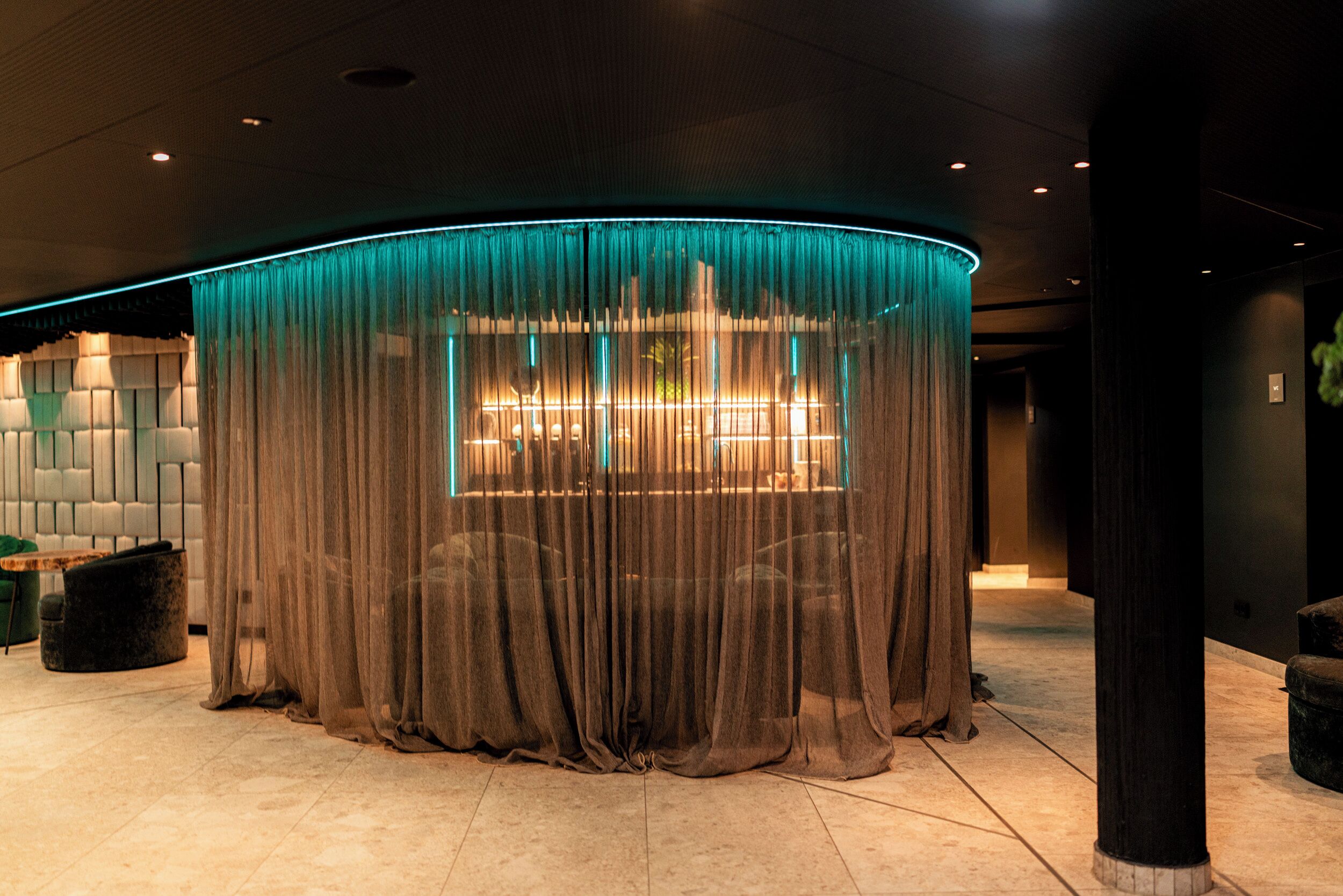 A lobby with a curved, illuminated structure, a seating area with a table and chairs, and a large window with curtains.