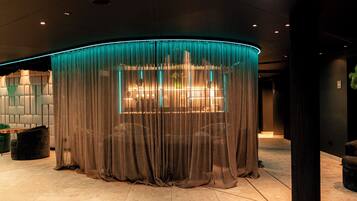A lobby with a curved, illuminated structure, a seating area with a table and chairs, and a large window with curtains.