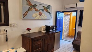 Une cuisine équipée d’un four à micro-ondes, d’une machine à café et agrémentée d’un vase de fleurs. Un tableau représentant des colibris est accroché au mur.