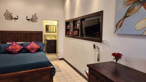Une chambre à coucher comprenant un lit, une commode, une coiffeuse avec un miroir, un téléviseur et des œuvres d’art décoratives accrochées au mur.