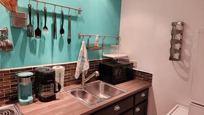 Une cuisine équipée d’un évier, d’une machine à café, d’un four à micro-ondes et d’ustensiles de cuisine accrochés au mur.