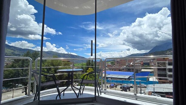 Varanda com mesa e cadeiras, com vista para uma paisagem montanhosa e o horizonte urbano.