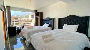 Quarto de hotel com duas camas, vista para montanhas e varanda.