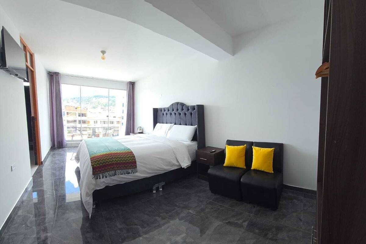 A hotel room with a bed, a bedside table, a chair, and a view of the outside.