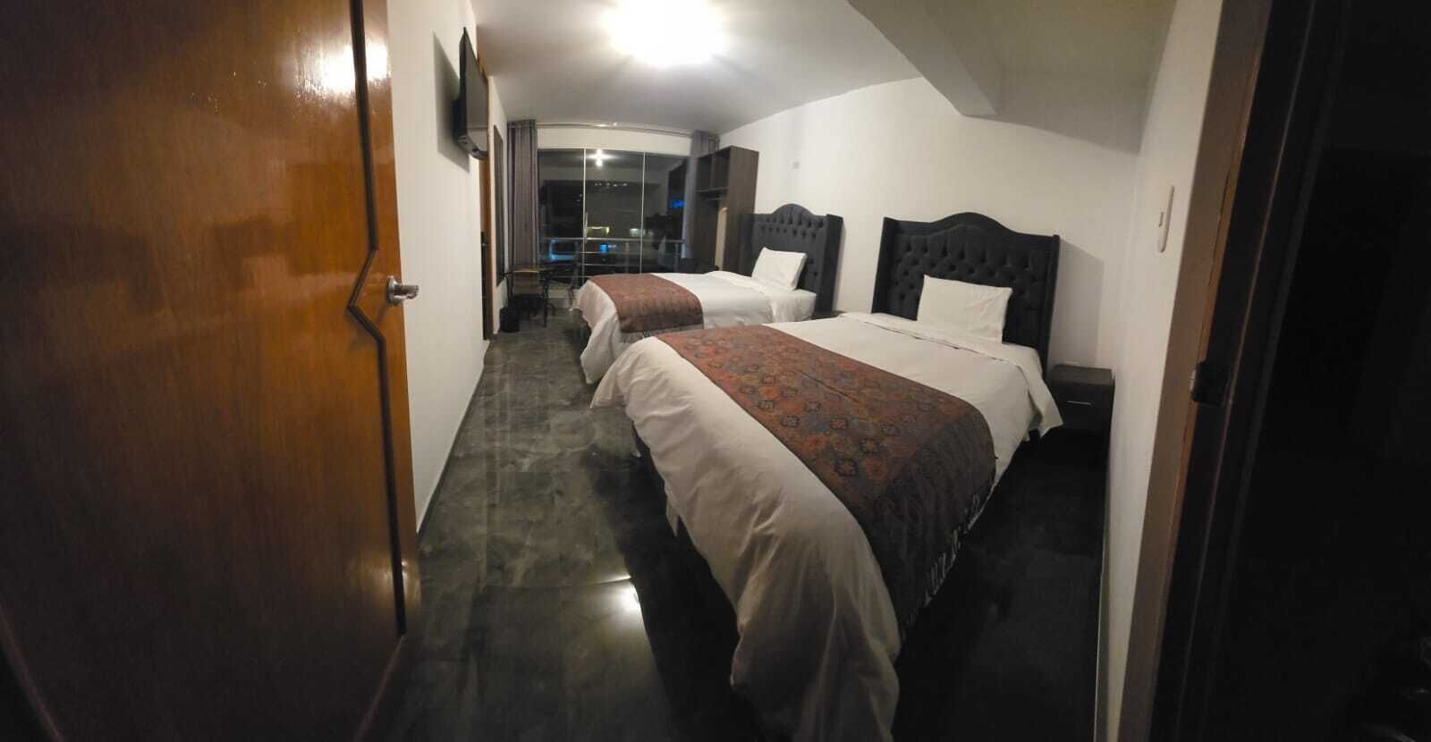 A hotel corridor with two beds, a TV, and a view of the outside.