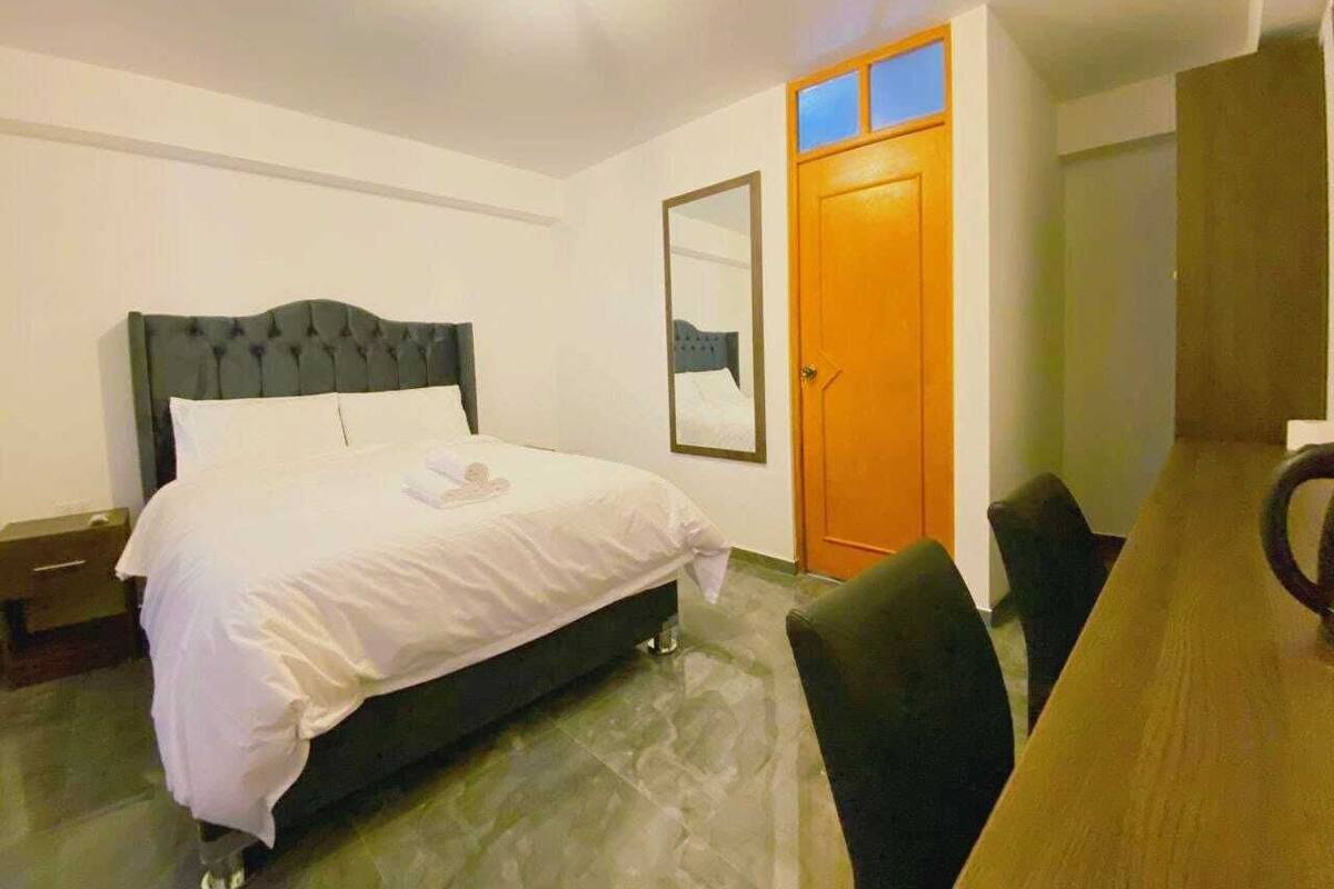 A bedroom with a bed, a wooden door, a mirror, and a dining table with chairs.