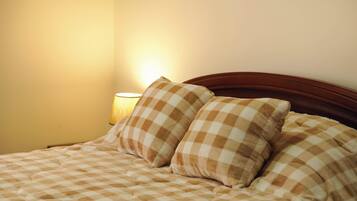 Una cama con colcha a cuadros y dos almohadas, una lámpara de noche y un cabecero de madera.
