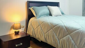 Ein Schlafzimmer mit Bett, Nachttisch mit Lampe, Wandbild und Holzboden.