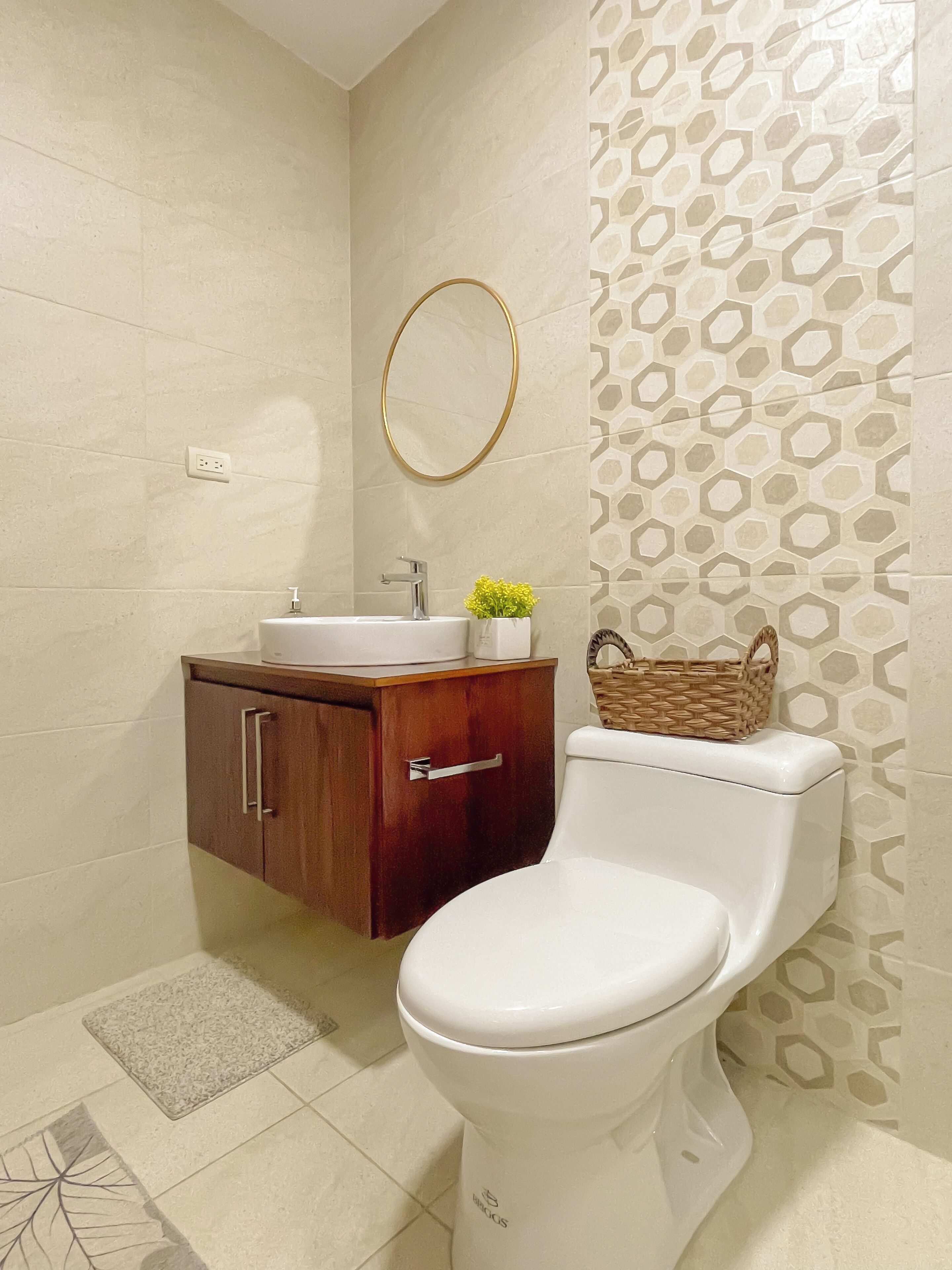 Een badkamer met een toilet, een houten kastje met een wastafel, een spiegel aan de muur en een behang met een patroon.