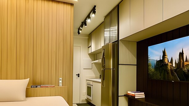 A bedroom with a bed, a TV mounted on the wall, a kitchen area, and a wooden panel wall. - Clementino 210 (São Paulo)
