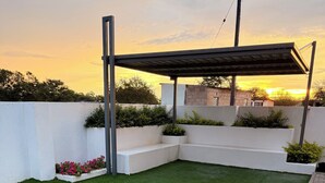 Un espacio exterior ajardinado con césped artificial, paredes blancas y una estructura de pérgola.