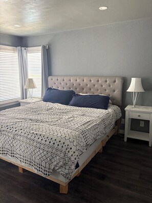 A bedroom with a tufted headboard, a patterned bedspread, two pillows, a nightstand with a lamp, and a window with curtains. - Vegas Hideaway conveniently located from airport and strip 8-20 minutes. . . (Las Vegas)