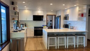 A modern kitchen with white cabinetry, a central island with bar stools, a built-in microwave, and a stainless steel refrigerator.