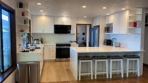 Una cocina moderna con armarios blancos, una isla central con taburetes de bar, microondas integrado y un refrigerador de acero inoxidable.