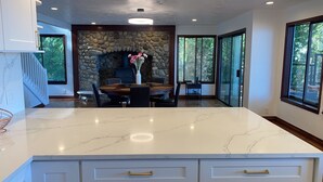 A modern kitchen with a stone fireplace, a dining area, and large windows.