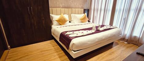 A hotel room with a large bed, wooden flooring, a headboard, and a wardrobe.