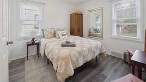 A bedroom with a bed, a nightstand, a mirror, and a window with blinds. - Airport Getaway -2BR near Detroit sports & events 20 min from Downtown A2 (Taylor)