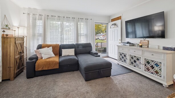 A living room with a sectional sofa, a flat-screen TV, a wooden cabinet, and a large window with curtains. - Airport Getaway -2BR near Detroit sports & events 20 min from Downtown A2 (Taylor)