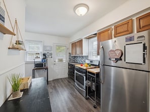 A compact kitchen with a microwave, stove, and refrigerator, wooden cabinets, and a hanging plant.