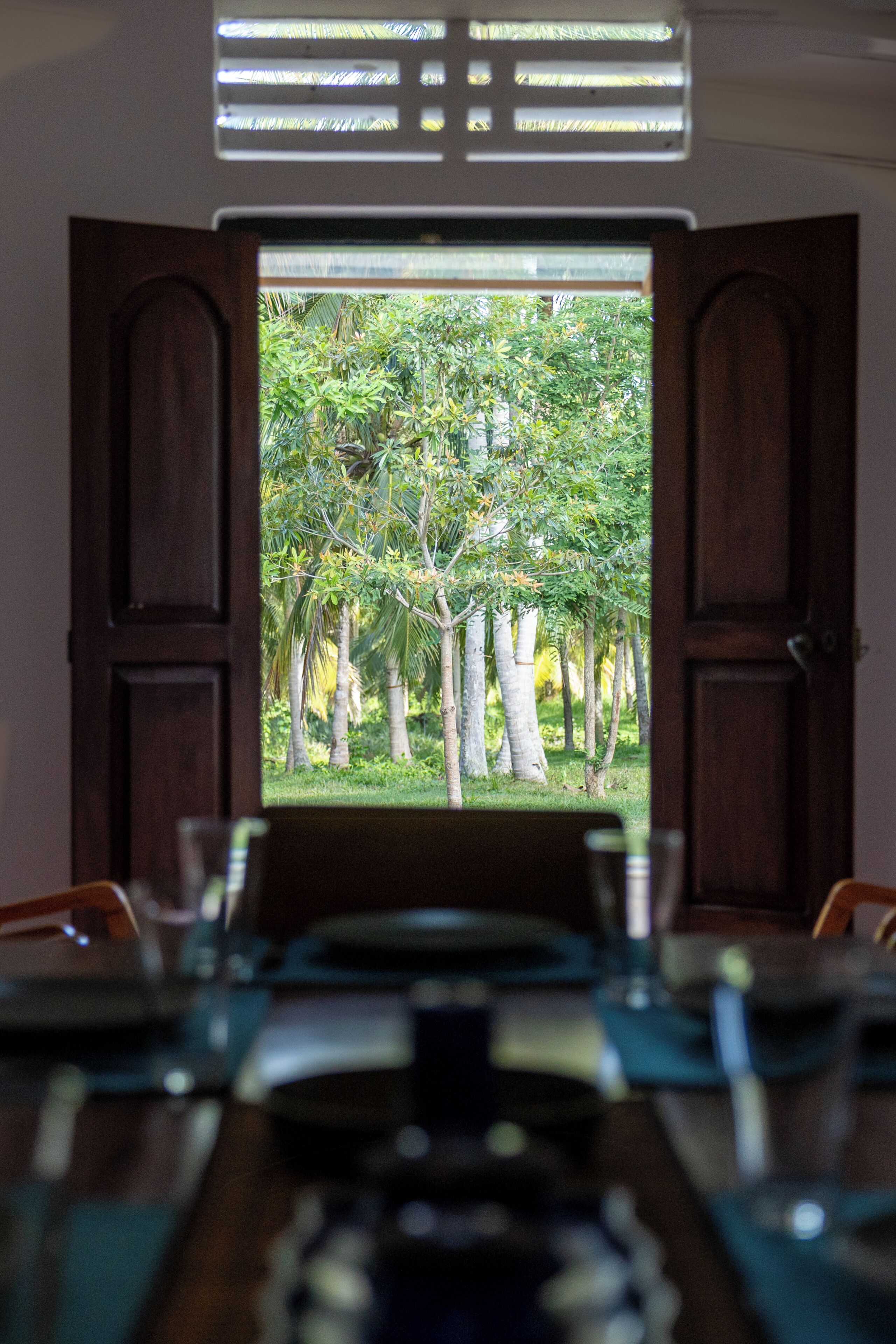 Une porte en bois ouverte donne sur un jardin luxuriant, avec des arbres et une table dressée pour le repas.