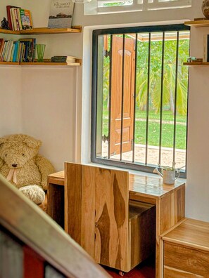 Une pièce avec un bureau en bois, une grande fenêtre donnant sur une porte en bois et sur la verdure à l’extérieur.