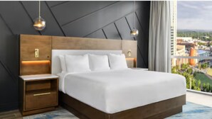 Una habitación de hotel moderna con una cama grande, cabecera de madera, mesitas de noche y vistas a la ciudad.