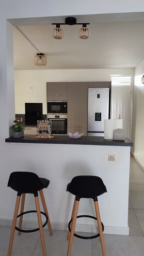 Eine moderne Küche mit einer zentralen Kochinsel, zwei schwarzen Barhocker, einem Kühlschrank und einer Mikrowelle.