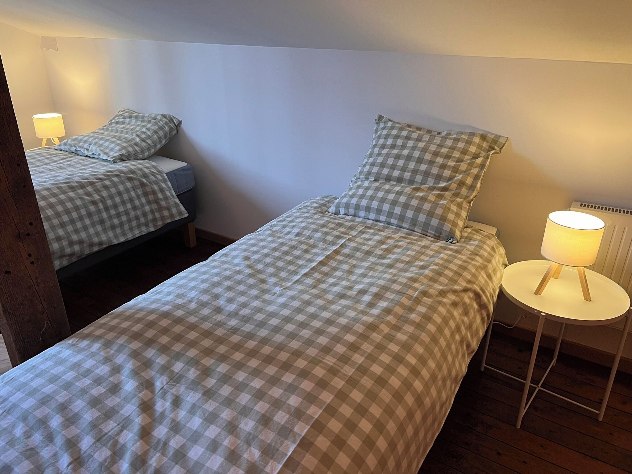 Quarto com duas camas, cada uma com roupa de cama xadrez, uma mesa de cabeceira com abajur e um radiador.