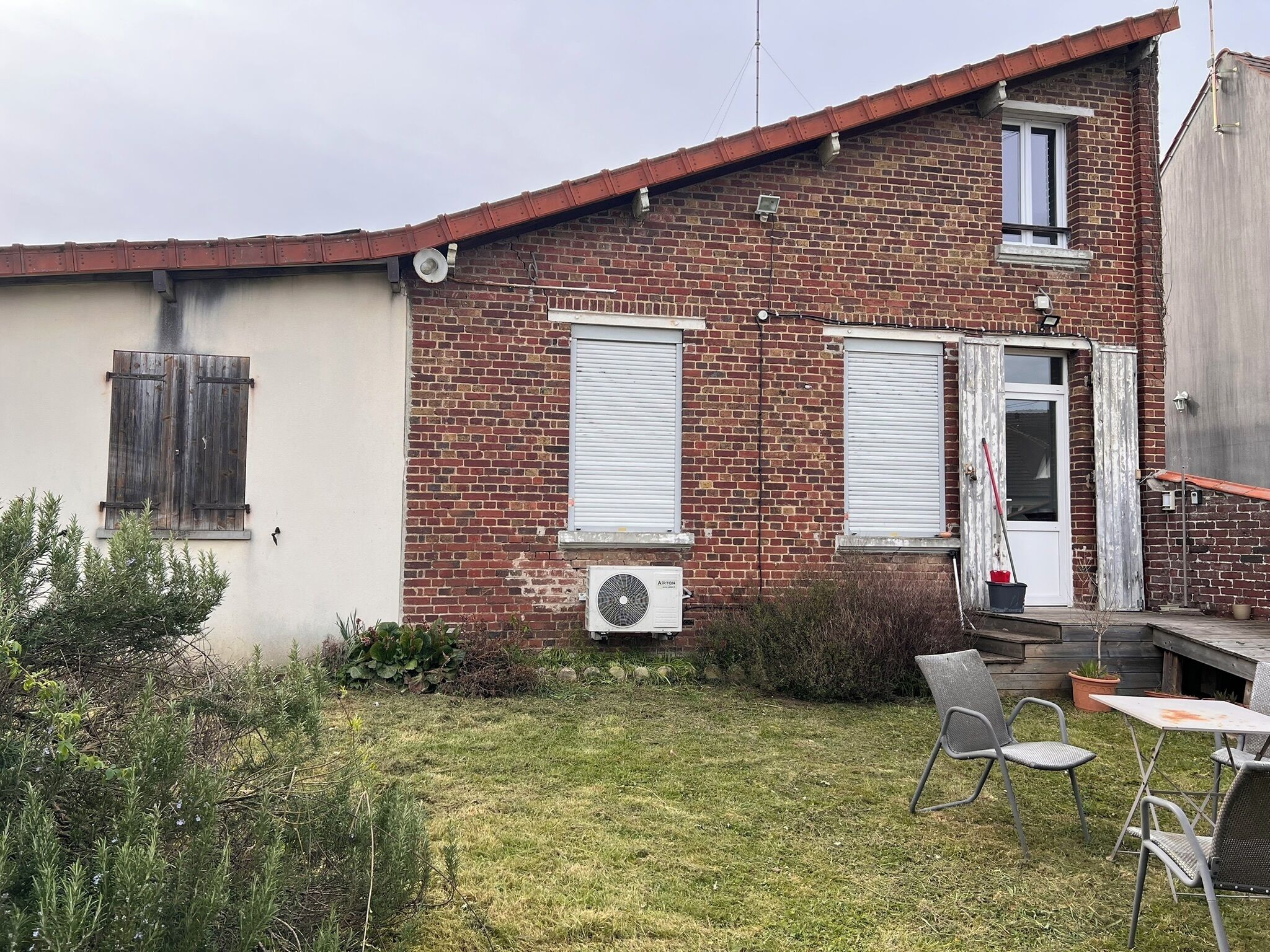 Ein Backsteinhaus mit einer kleinen Terrasse, einer weißen Tür und einem Fenster mit Rollläden.