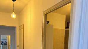 Un pasillo con piso de madera, un accesorio de iluminación y una puerta entreabierta que da a un baño con bañera.