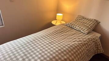 Una cama individual con una colcha a cuadros, una lámpara de noche y una almohada.