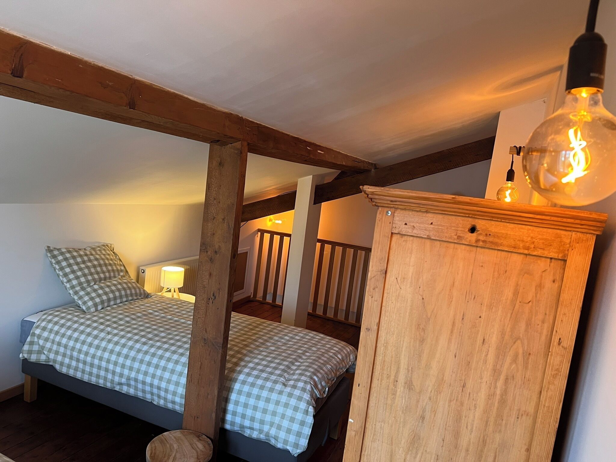 A bedroom with a checkered bedspread, a wooden headboard, a nightstand with a lamp, and a hanging light fixture.