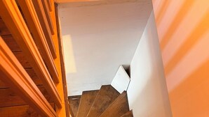 Una escalera de madera con barandilla que lleva a un rellano con pared blanca.