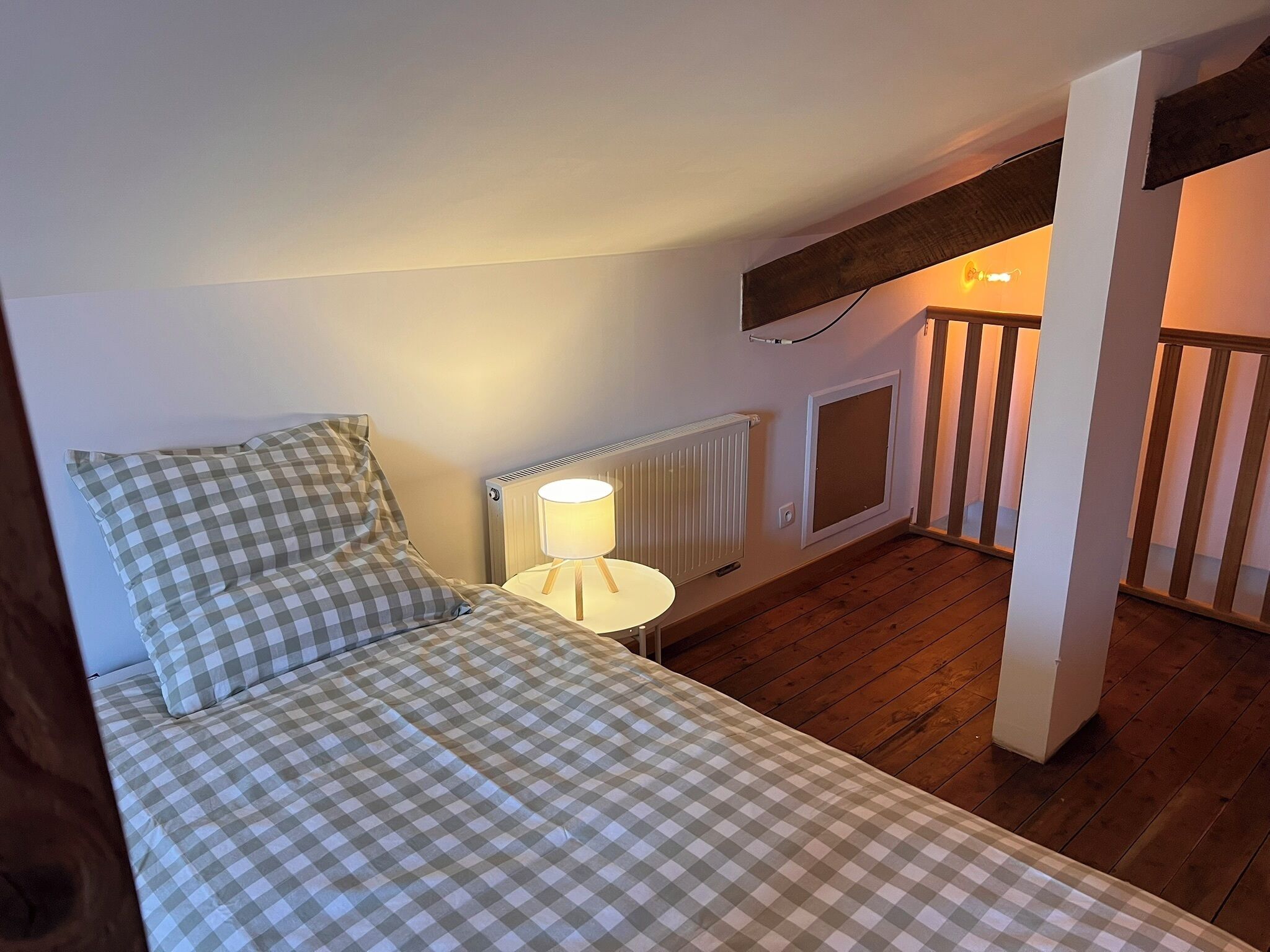 Een slaapkamer met een geruit beddegoed, een bedlamp, een radiator en een houten vloer.
