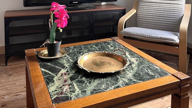 Un salón con televisión de pantalla plana, un sillón acolchado, una mesa de centro con un plato decorativo y una orquídea en maceta.