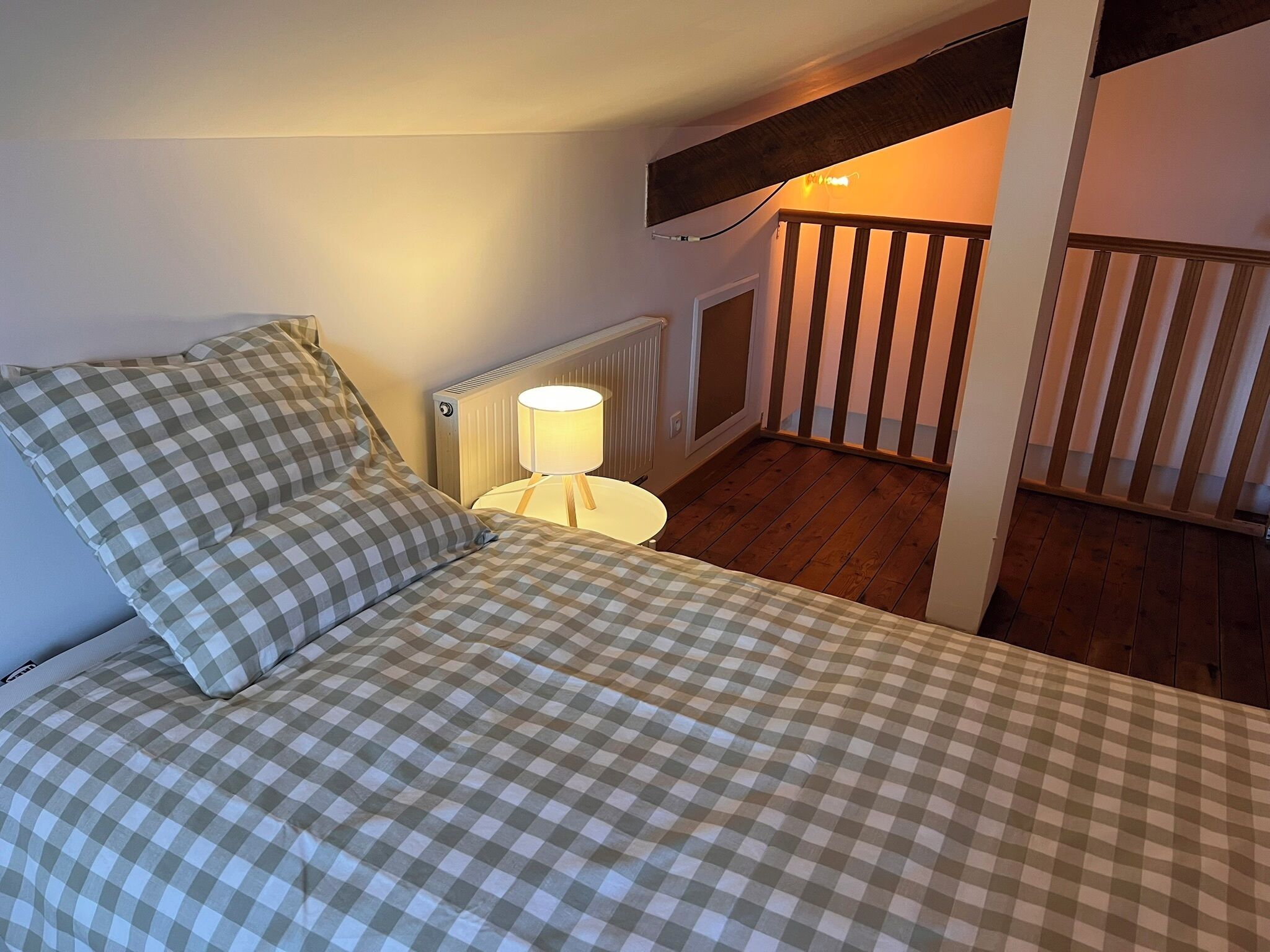 Una camera da letto con copriletto a quadretti, una lampada da comodino, un termosifone e una scala in legno.