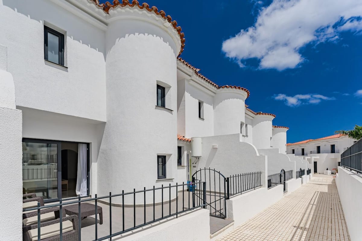Un bâtiment blanc doté de balcons, d’un toit recouvert de tuiles et surplombant un ciel d’un bleu limpide.