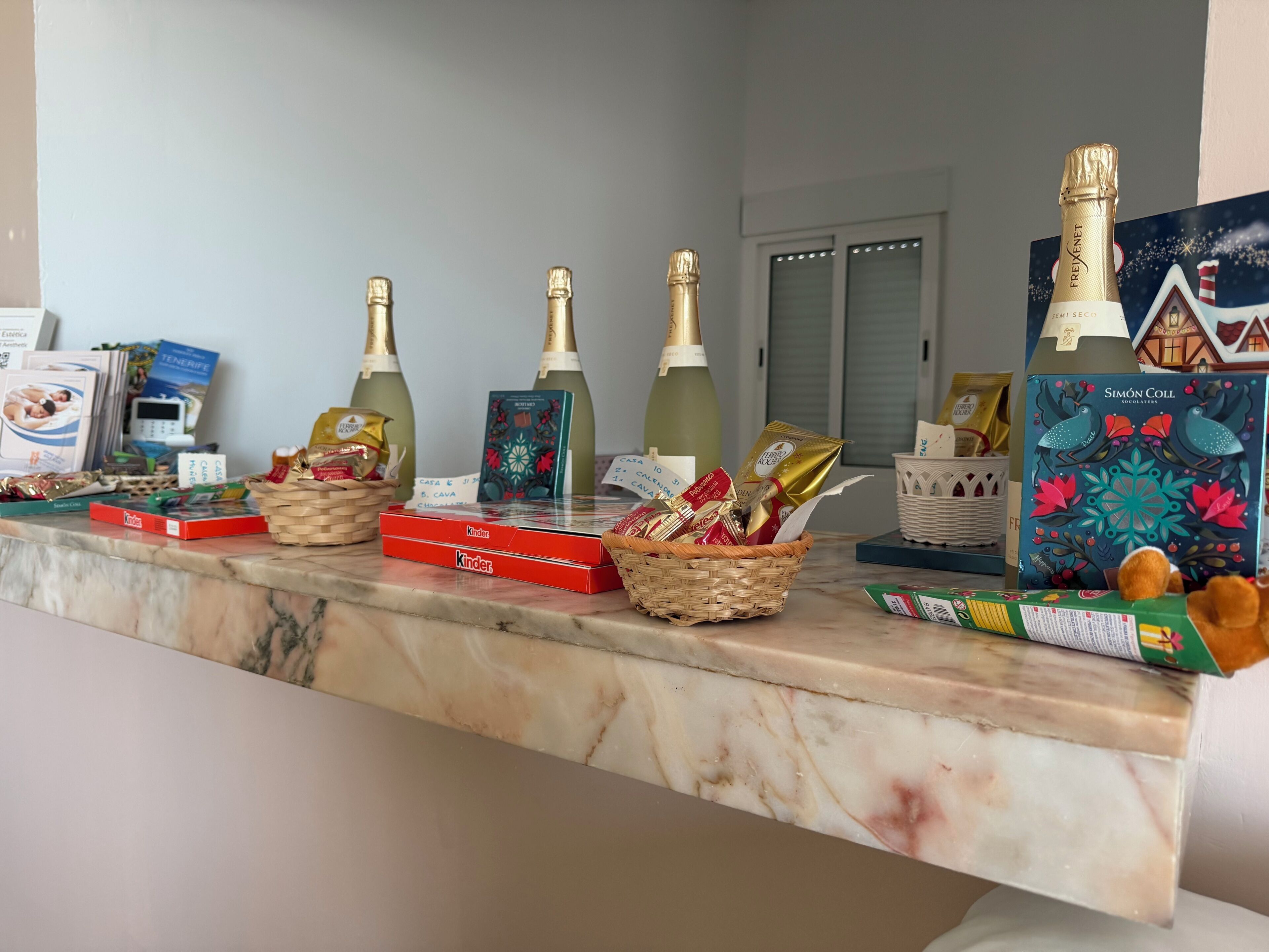 Una encimera de mármol con varios artículos, incluyendo cajas de chocolate Kinder, una cesta de bombones y botellas de champán.